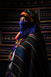 Portrait artistique d’une femme amazighe d’Agoudal, vêtue d’un manteau rayé et d’un foulard traditionnel, lumière douce.